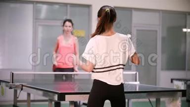 打乒乓球。 年轻女子和她的朋友打乒乓球。 背面