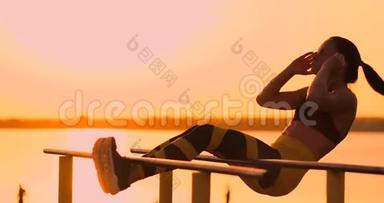 腹部肌肉锻炼。 日落时分，一位年轻的美女在湖边运动，一位穿着运动服的夏日女子在做运动