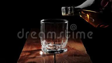 豪华威士忌。 手把<strong>金色</strong>的威士忌从一个方形的<strong>瓶子</strong>倒入一个玻璃在棕色的木制桌子上的黑色背景。
