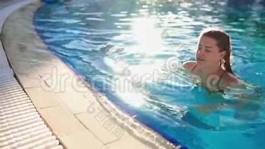 在阳光明媚的一天，女人在游泳池里用蓝色透明的水游泳，放松游泳池，水