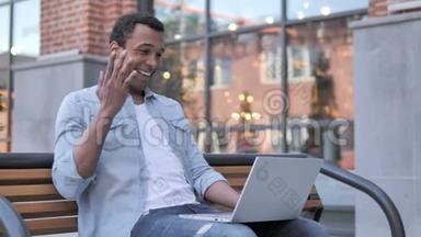 坐在长凳上的非洲男人在笔记本电脑上在线视频聊天