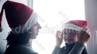 快乐的家庭妈妈和宝宝在家玩白色窗户过圣诞节。 穿圣诞老人帽子的快乐男孩和女人。