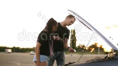 一对年轻夫妇的侧视图停在了停车场的路上。穿黑色T恤的年轻人检查<strong>机油</strong>
