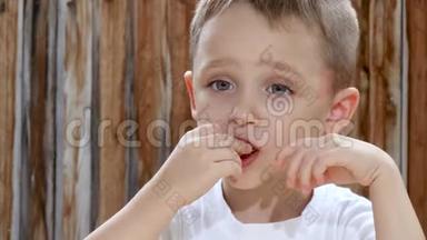 一个孩子在木墙的背景下坐在一张桌子旁，一边高兴地吃薯片。 特写镜头。