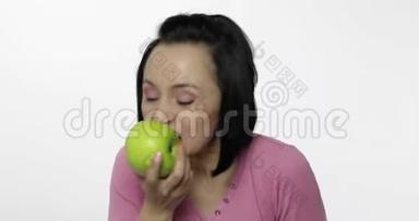 年轻漂亮的女人在白色背景下吃着大而多汁的绿苹果