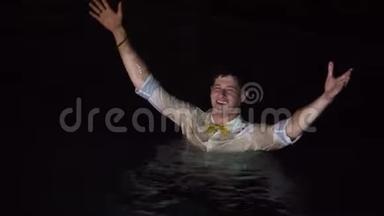 一个年轻人穿着衬衫和其他衣服在游泳池里洗澡。 晚上在热带别墅聚会。 喝醉了洗澡。