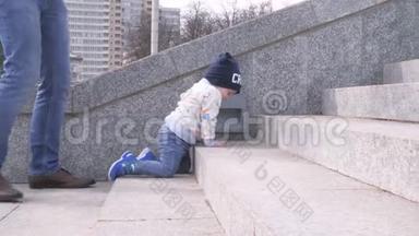 小男孩正在城市公园的花岗岩楼梯上爬，他<strong>父亲</strong>把孩子扶起来，<strong>帮助</strong>他度过一个阳光明媚的日子