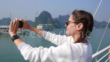 年轻女子穿着白色毛衣和太阳镜，带着智能<strong>手表</strong>，站在智能<strong>手机</strong>上拍摄海湾的照片