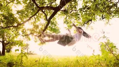 美丽的女孩在被阳光照亮的秋千上摆动。 绳子在公园的树枝上摆动。 慢动作。