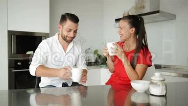 年轻夫妇在现代厨房吃早餐。 白色咖啡杯。 早上吃早餐。 幸福的妻子和丈夫。 浪漫浪漫