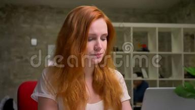 放松的浓白白种人姜女正在电脑上打字，坐在室内，桌面上，富有创意的现代