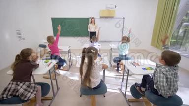 一群小学生在上课时举手回答问题，坐在教师面前的课桌前上小学