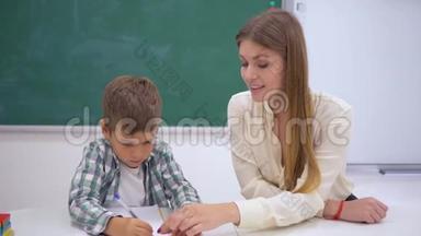 小学，专业家教在黑板边的桌子上帮助学生学习写字