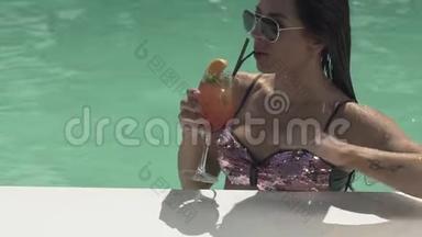 戴太阳镜的漂亮女人正站在游泳池里喝她的鸡尾酒。 穿比基尼的孤独女士的休闲。
