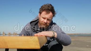 有胡子和胡子的木匠在蓝天上触摸桌子的表面，由他<strong>手工</strong>制作。 <strong>手工手工</strong>制作