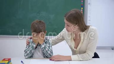 在学校教室黑板旁的课桌上，亲切的老师在课外活动中安抚哭泣的学者男孩