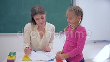<strong>孩子</strong>们<strong>上学</strong>，微笑的女教育家在教室黑板附近的桌子上检查小女孩的家庭作业
