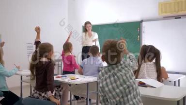 老师站在教室前面，靠近黑板，向学生们<strong>提问</strong>他们是向谁<strong>举手</strong>的