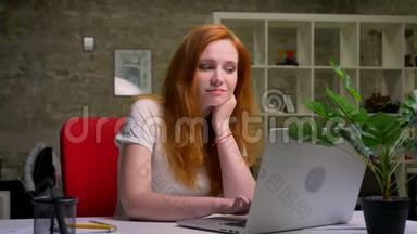 一个可爱、体贴、红发白种人的女人坐在电脑前微笑着写着笔记