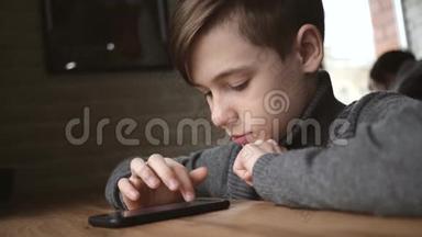 十几岁的男孩坐在窗边的咖啡馆里，手里拿着一部智能手机。 社交网络中的交流。 运动会