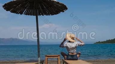 穿着衬衫戴着帽子的女孩坐在沙滩上的遮阳伞下