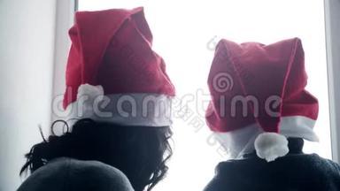 快乐的家庭妈妈和宝宝在家玩白色窗户过圣诞节。 穿圣诞老人帽子的快乐男孩和女人。