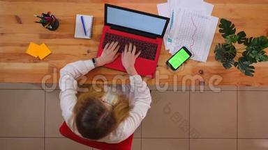 为年轻的白种人员工拍摄的特写镜头，他们使用笔记本电脑，桌上放着绿色屏幕的手机