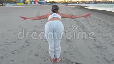 年轻女子正在做瑜伽，在日出时在沙滩上站立弯曲的波塞。