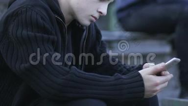 青少年男孩坐在户外玩智能手机游戏，玩电子游戏成瘾