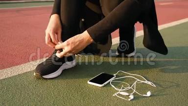 年轻的运动员女人把跑鞋和耳机绑在地上。 关门