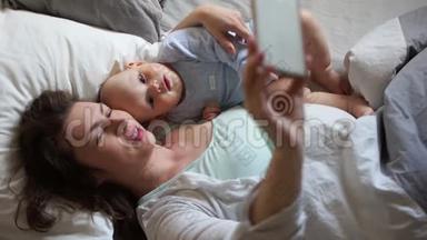 妈妈和<strong>宝宝躺</strong>在床上自拍。母亲节，家人早上好，智能手机和<strong>宝宝</strong>