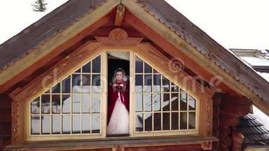 无人机的镜头从美丽的新娘身上飞过，她站在木屋的阁楼上，露出了那座山