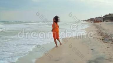 一个穿着<strong>橘色</strong>连衣裙的漂亮女人在潮湿的海滩上奔跑