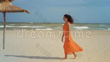 穿着橘色连衣裙戴着太阳镜的美女赤脚踏上沙滩，来到风和日丽的天气