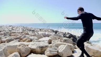 年轻健康的运动员在海滩的岩石上奔跑和跳跃，强烈的海浪拍打着悬崖和溅起的水花。