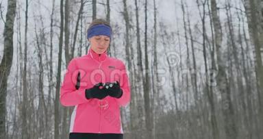 一位正在晨间慢跑的年轻女子手里拿着一部智能手机，挑选一首音乐曲目进行训练。冬季跑步。使用