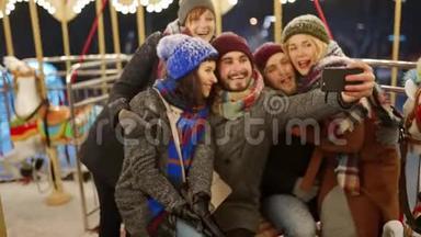 快乐的人在新年冬展游乐园的智能手机相机上自拍。 微笑的朋友很开心