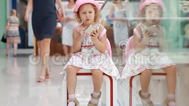 女孩在购物中心玩手机。 婴儿在智能手机上使用游戏应用程序