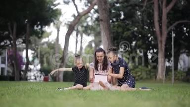 母女俩在草地上用药片。 妈妈在草地上给两个女儿读故事