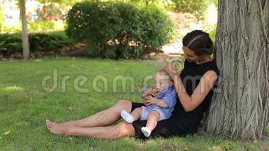 快乐的妈妈和她新生的儿子<strong>坐在</strong>一棵<strong>树下</strong>的夏天公园里。