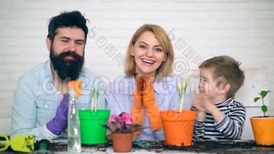 父亲、母亲和儿子正在手掌中拍手，看着摄像机旁边的花盆，里面放着刚开过的花