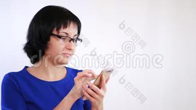 带眼镜的布鲁内特女孩在白色背景下使用智能手机。 女孩用手指触摸智能手机