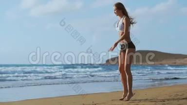 穿着运动服装短裤和t恤的女孩在加那利群岛海边的海滩上蹲着跳