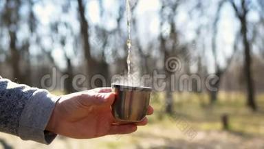 把热茶从热水瓶里倒入杯子里。 在森林里野餐大自然。