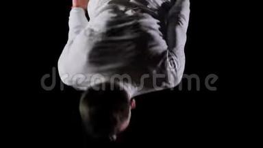 年轻英俊的男杂技演员穿着白色衣服在黑色背景下做跳跃和<strong>展示旋转</strong>技巧