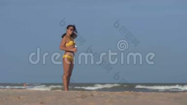太阳眼镜中的女人把头发随风<strong>飘摇</strong>，在沙滩上捧着一瓶水