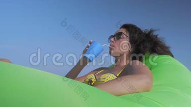 美丽的女人在比基尼饮料鸡尾酒放松在海上躺在海滩上的绿色充<strong>气垫</strong>小屋