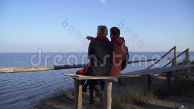 年轻夫妇坐在长凳上，拥抱在水面的背景上。 在户外约会的情侣