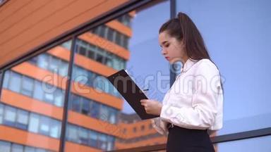黑发的商务女孩正在商务中心附近的工作文件中做笔记。 4K