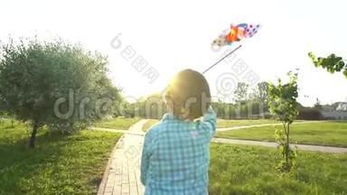 可爱的男孩手里拿着玩具风力涡轮机，在夕阳下的夏季公园跑步。 快乐的孩子，玩孩子，玩得开心